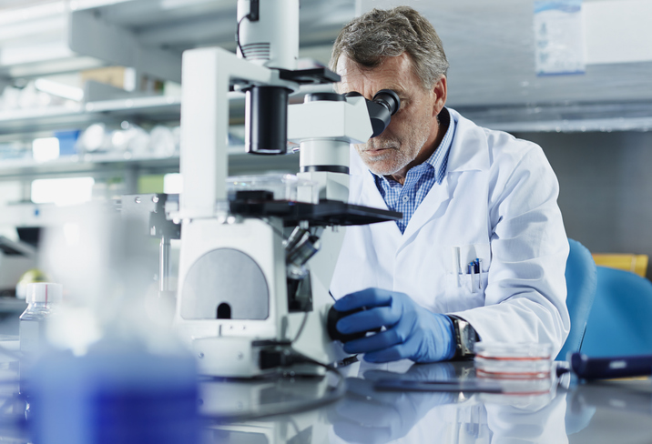 Photo shows a scientist looking through a microscope in research laboratory