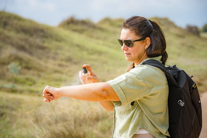 Woman spraying bug repellent on arm while hiking
