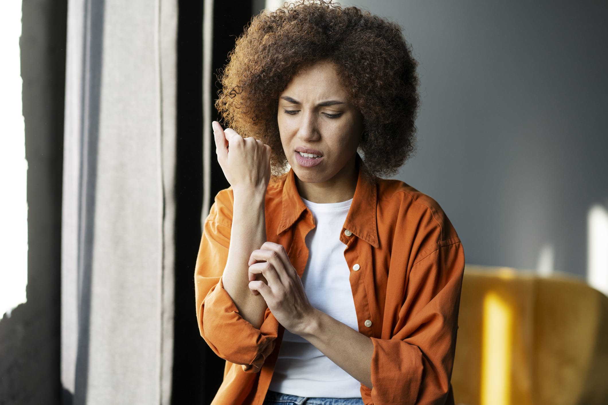 Photo of woman frowning while scratching arm