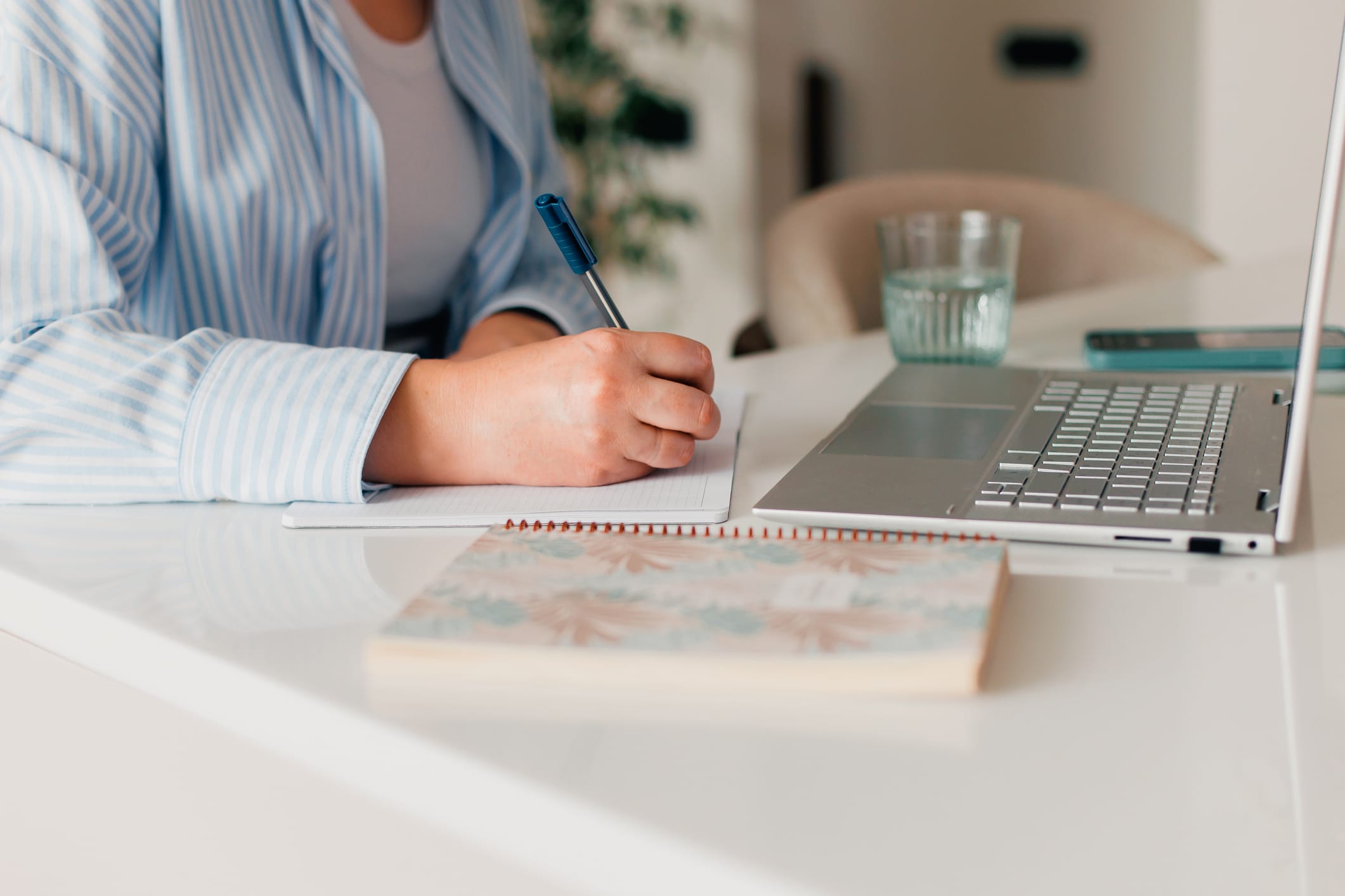 Woman sitting in front of laptop writing in a notebook