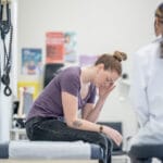 A young female sits up on an exam table as she talks with doctor