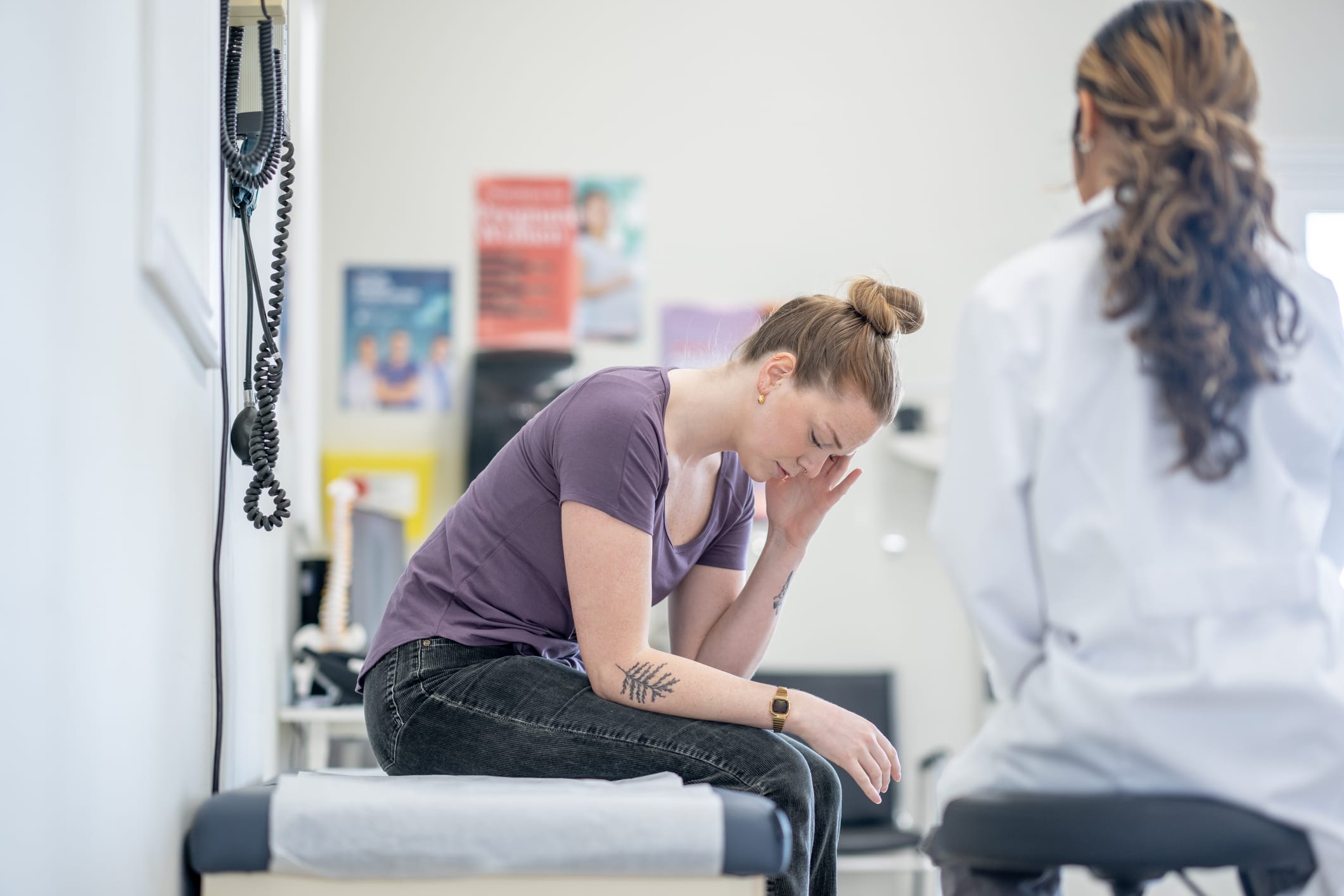 A young female sits up on an exam table as she talks with doctor