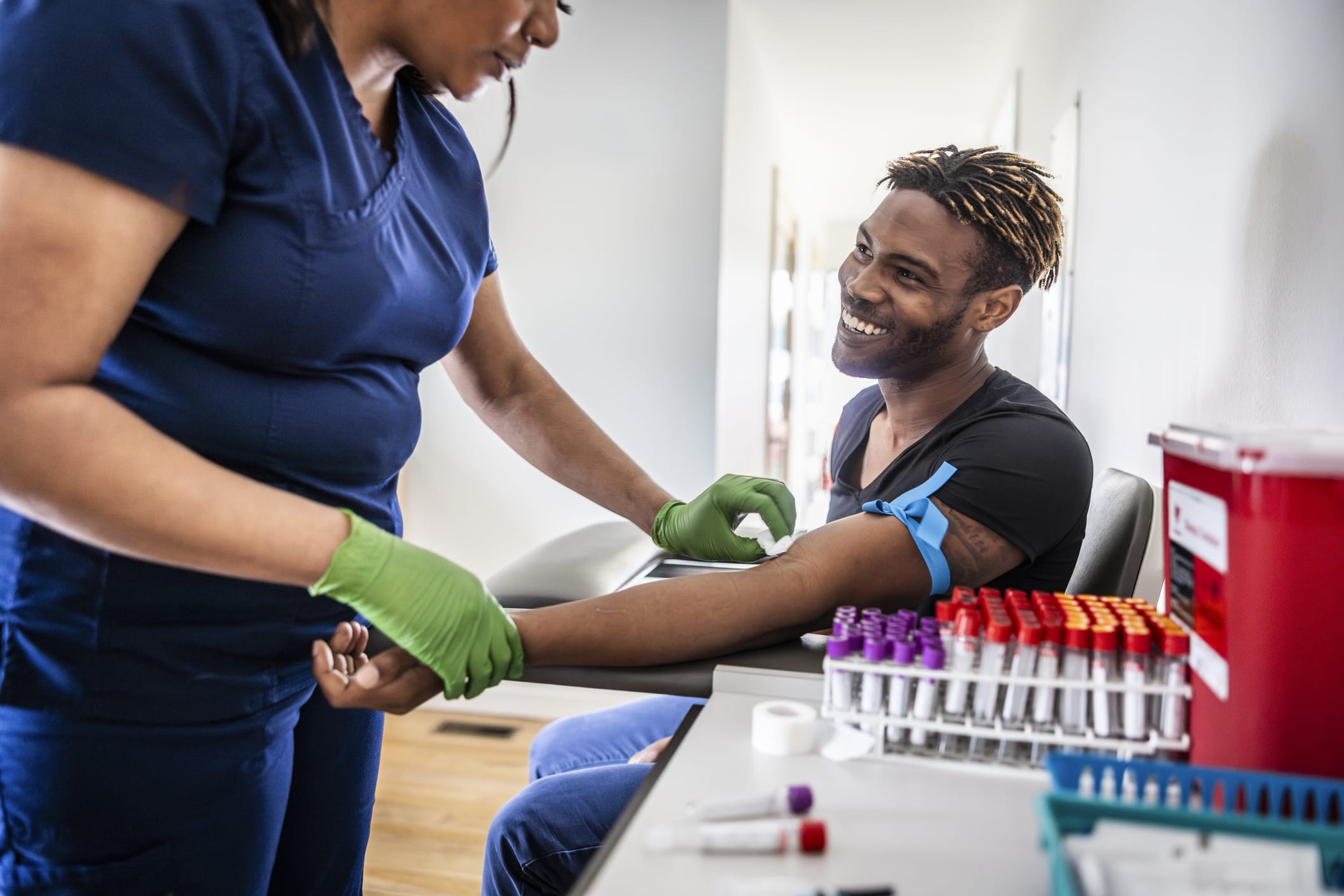 Female nurse drawing blood sample from young man in medical office