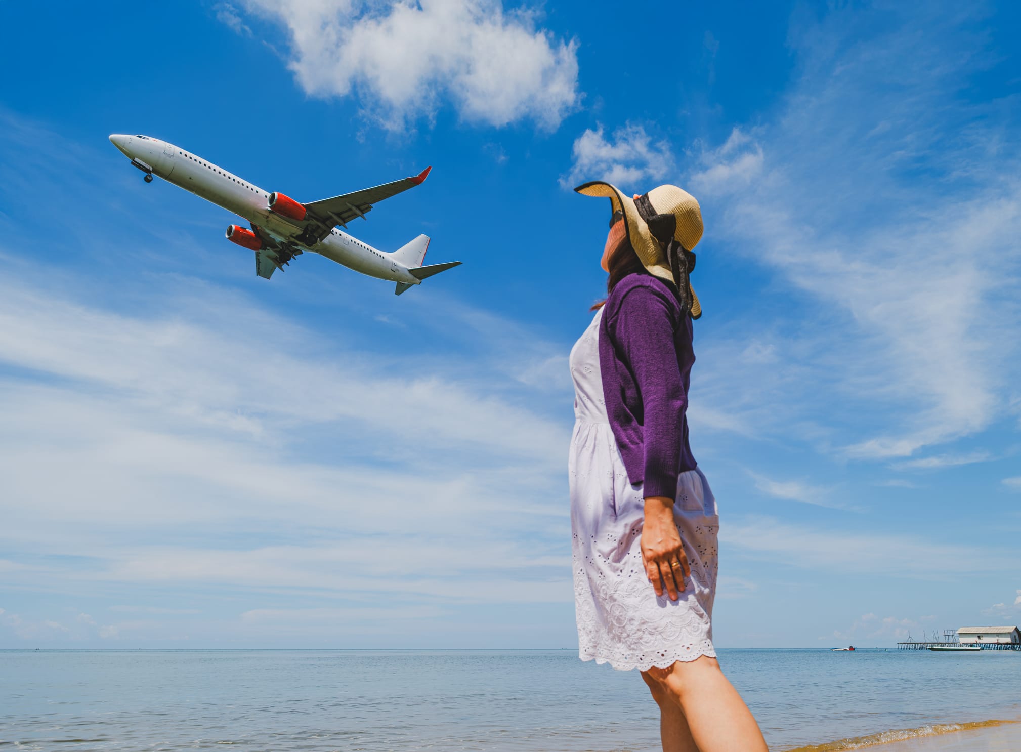Woman watching an airplane passing by near the beach