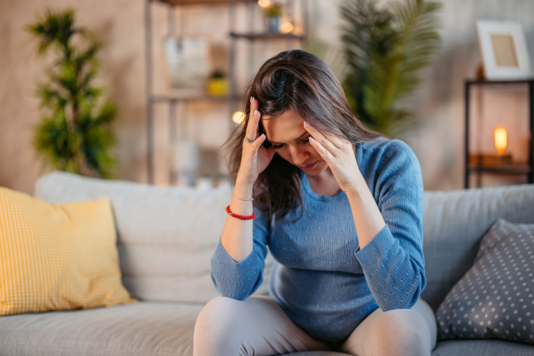 Young pregnant woman sitting on couch with head in hands