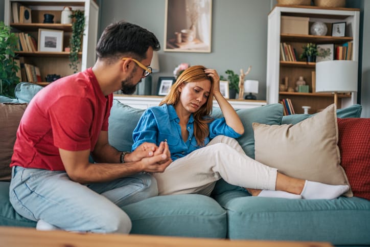 Young man holding his wife's hands while comforting her on the sofa