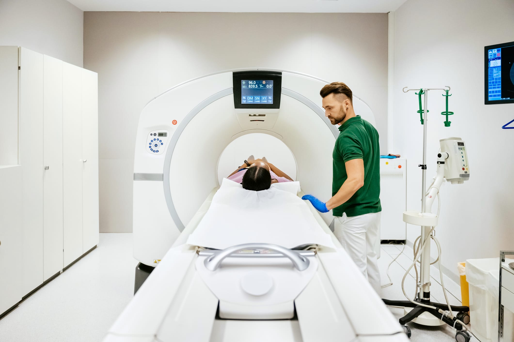 A frontal view of the mechanical bed attached to the orifice of a CT Scanner being operated by a hospital technician.