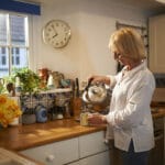 A senior woman pours a hot drink at home in the kitchen.