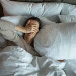 Woman in bed with hands over eyes