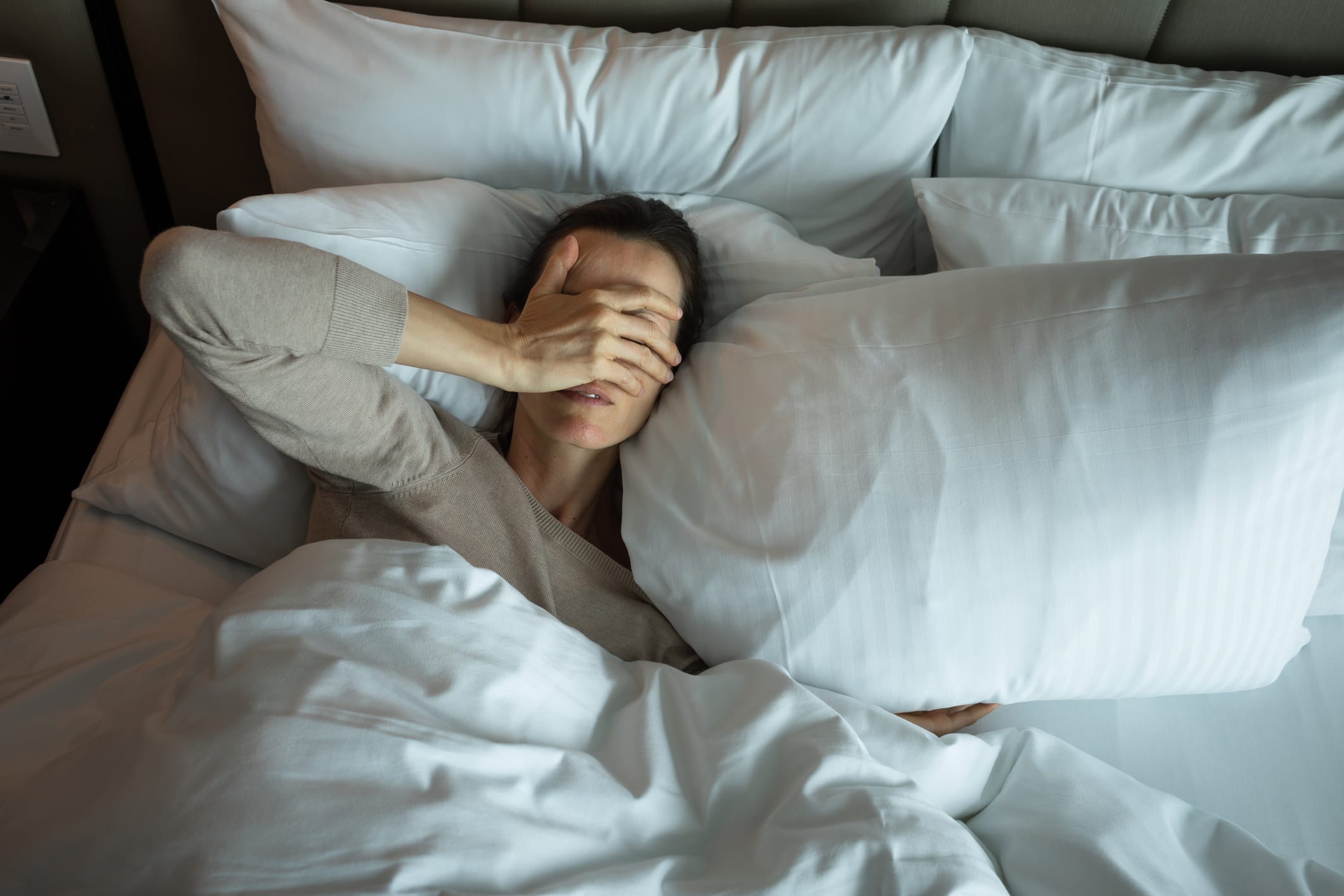 Woman in bed with hands over eyes