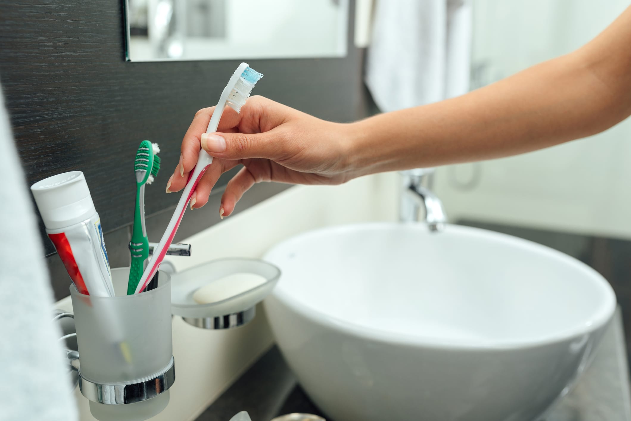 Close-up of a woman picking up a toothbrush to brush teeth