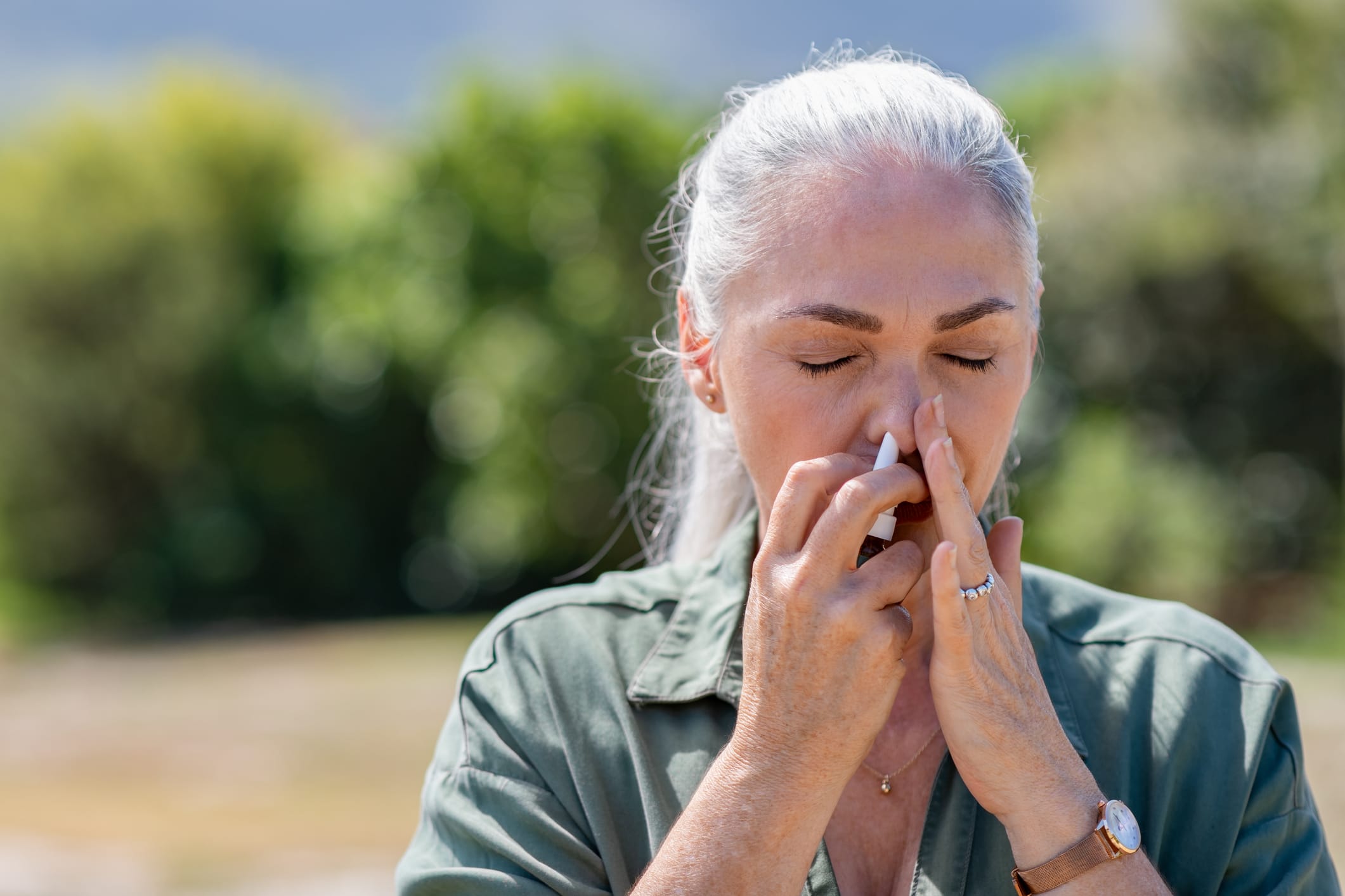 Older woman using nasal spray outdoors