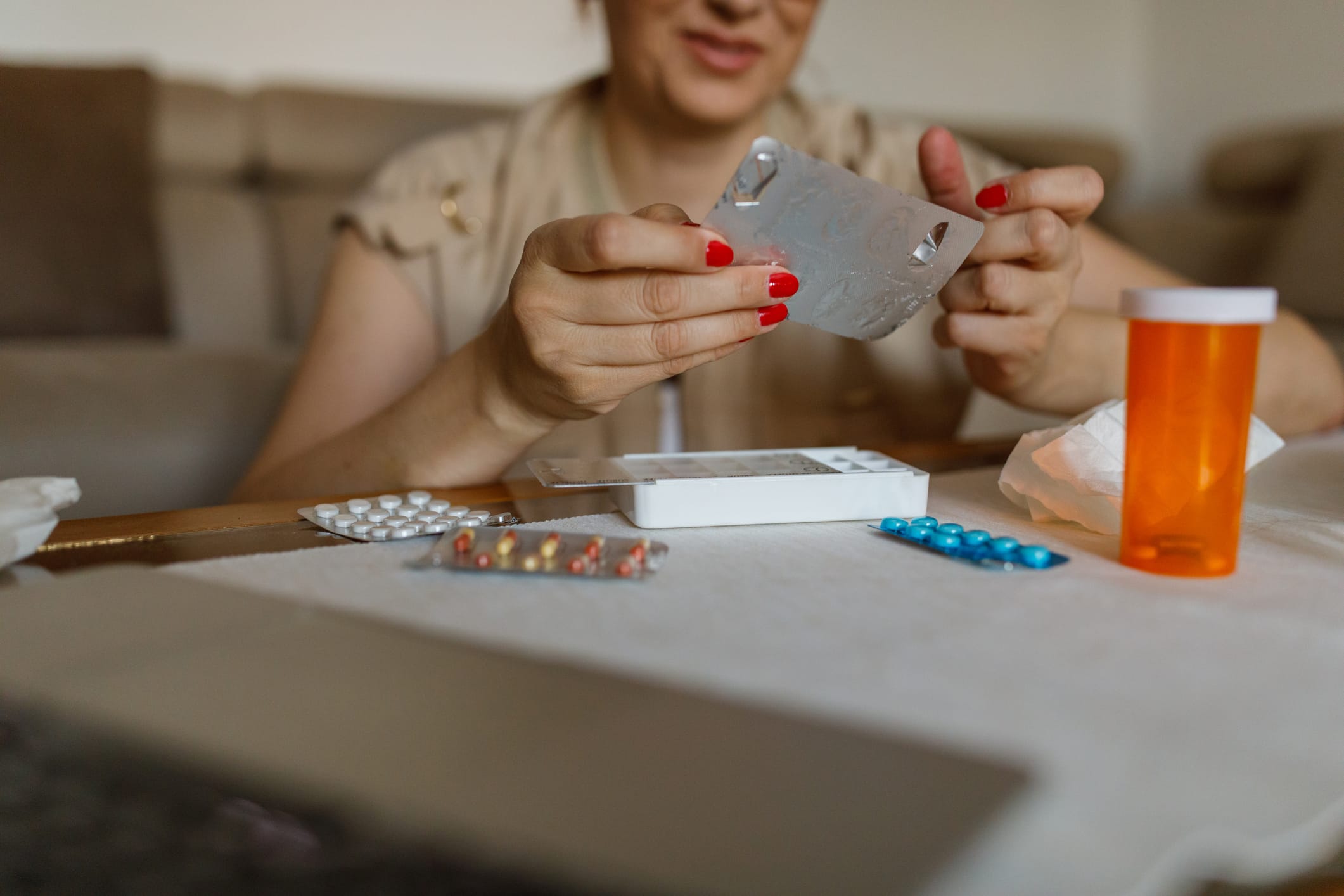 Selective focus shot of smiling mature woman sitting on the floor, at the coffee table, sorting out her prescription medication in a pill organizer.