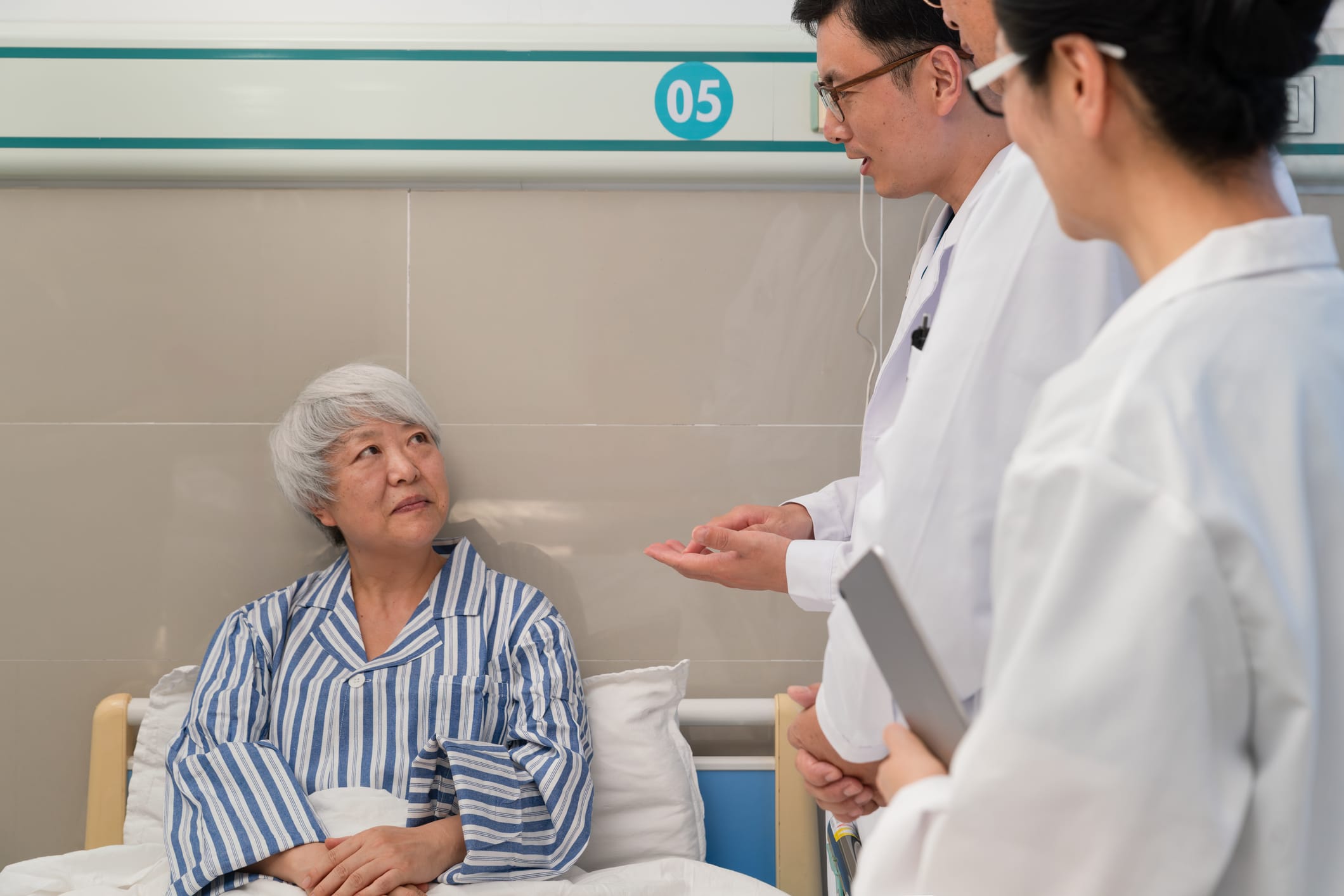 Doctors speak with an older woman in hospital bed