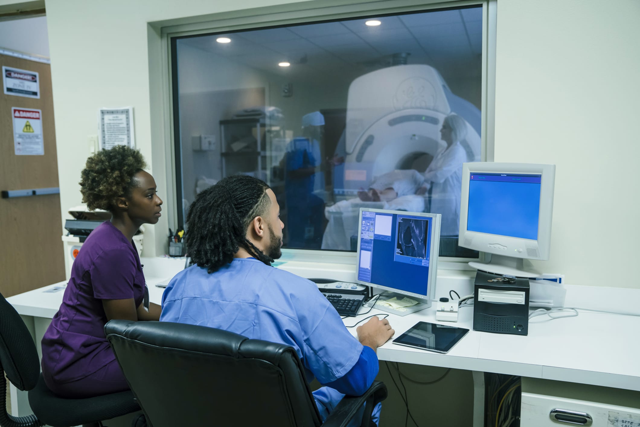 Nurses using computer near MRI with patient in background