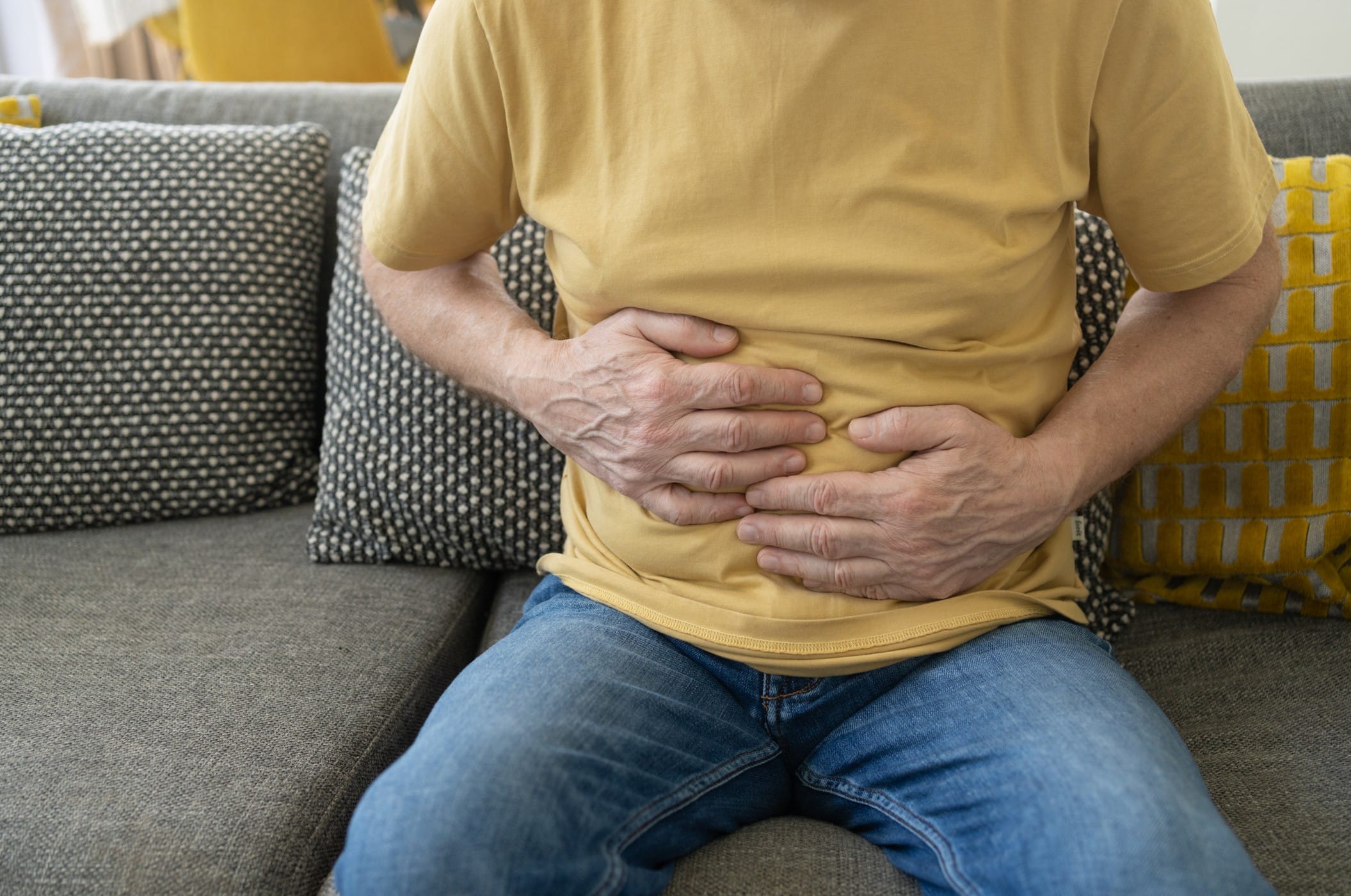 Seated man holding hands on stomach.