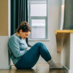 Woman seated on the floor and holding her stomach in pain