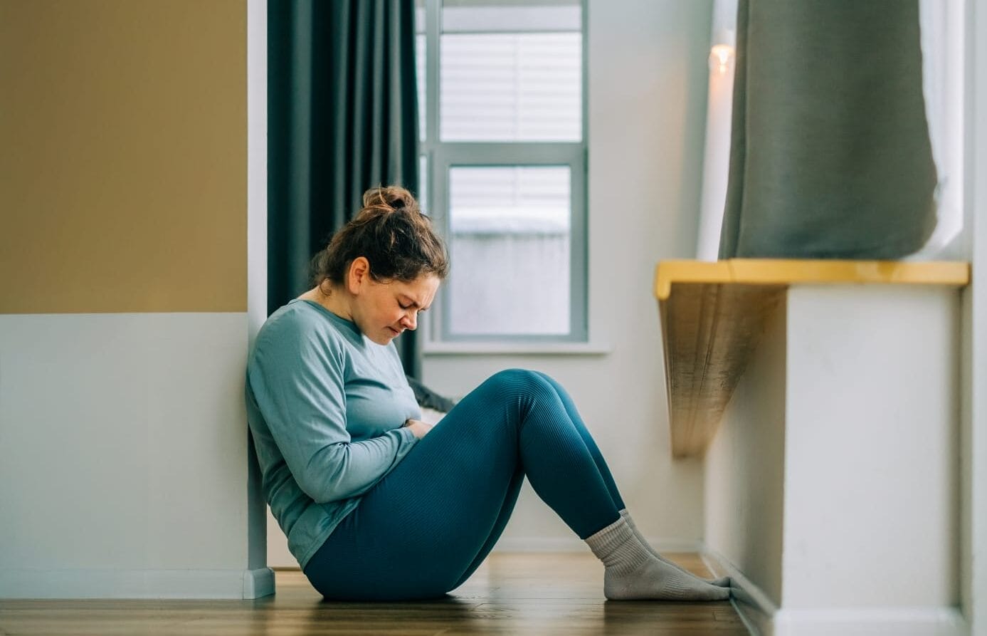 Woman seated on the floor and holding her stomach in pain